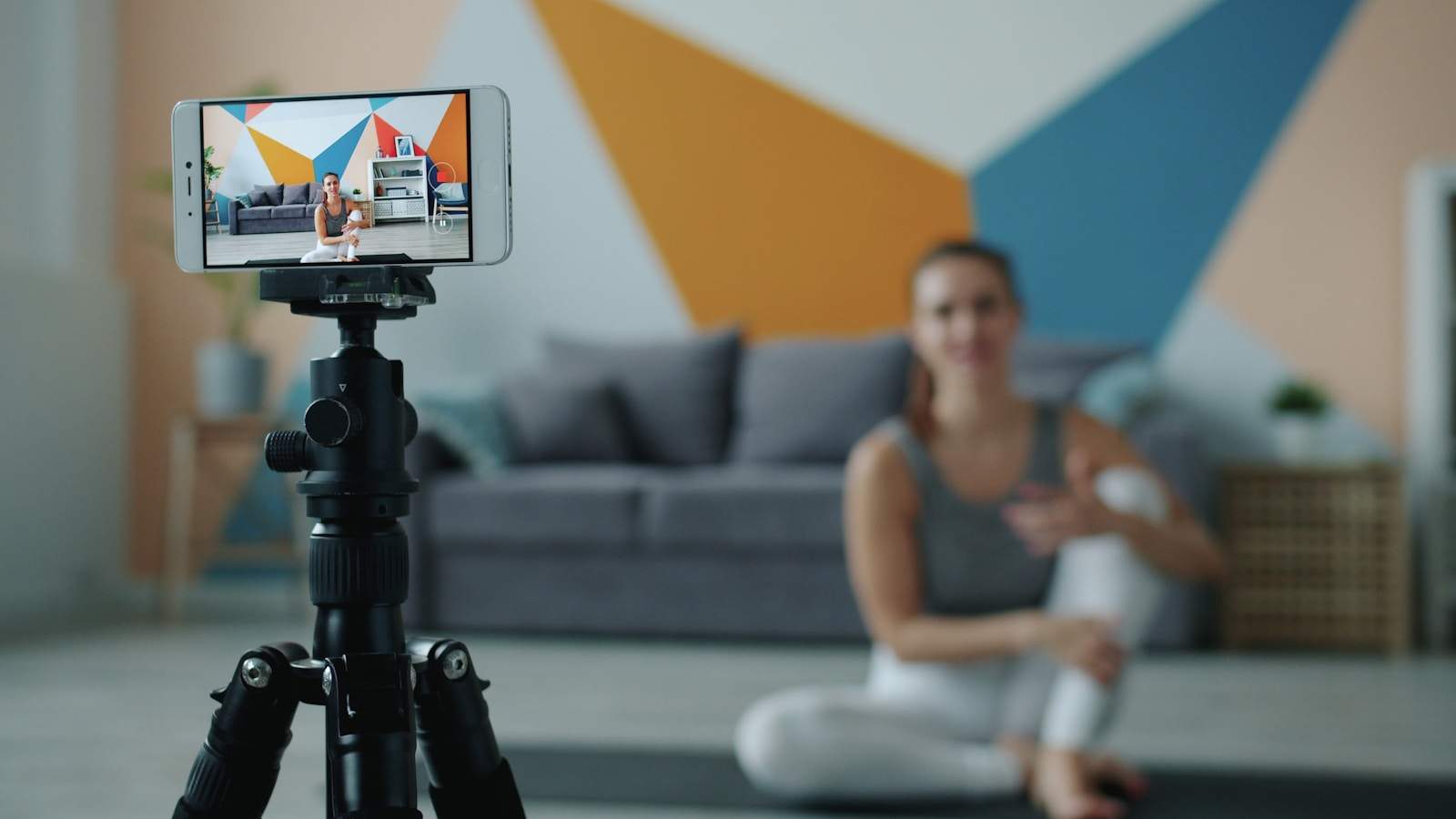 Woman recording fitness video on phone with tripod.